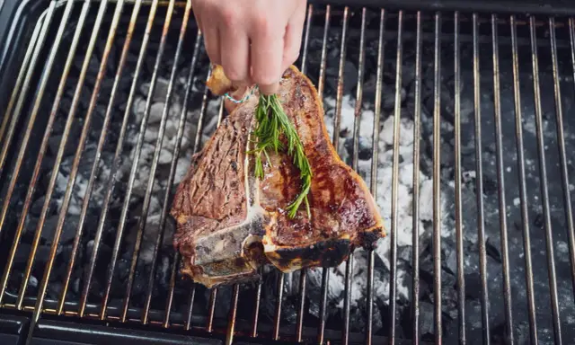 Ein saftiger florentiner steak wird mit Rosmarin auf dem Grill verfeinert.