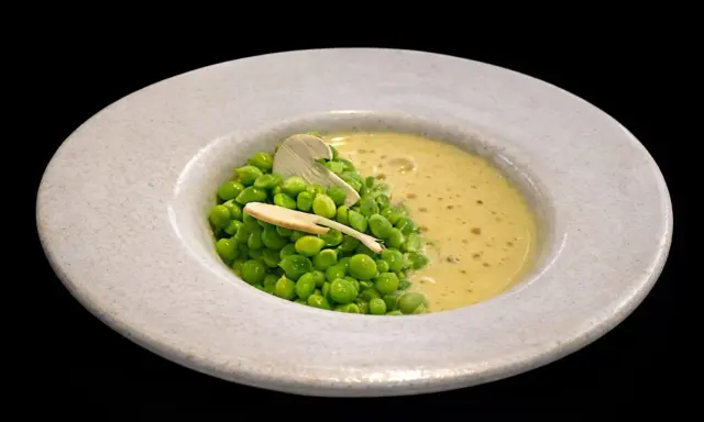 Un plato de guisantes de lágrima frescos con una cremosa sopa amarilla y una fina lámina de champiñón.