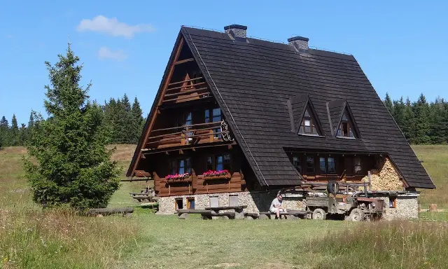 Drewniana bacówka na Krawcowym Wierchu, otoczona zielenią i lasem. Obok stoi stary traktor.