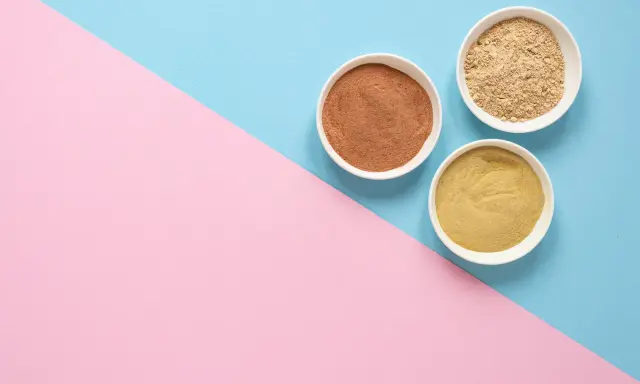 Tres cuencos blancos con polvos de diferentes tonos, como masilla para pared interior, sobre un fondo dividido en rosa y azul.