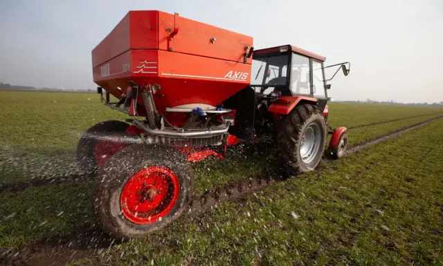 Czerwony traktor z rozsiewaczem nawozu na wiosennym polu. Odpowiedni nawóz pod warzywa na wiosnę to klucz do obfitych plonów.