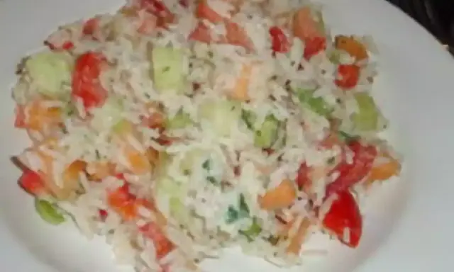 Une savoureuse salade de riz garnie de dés de tomates, de concombre et d'herbes fraîches, servie sur une assiette blanche.