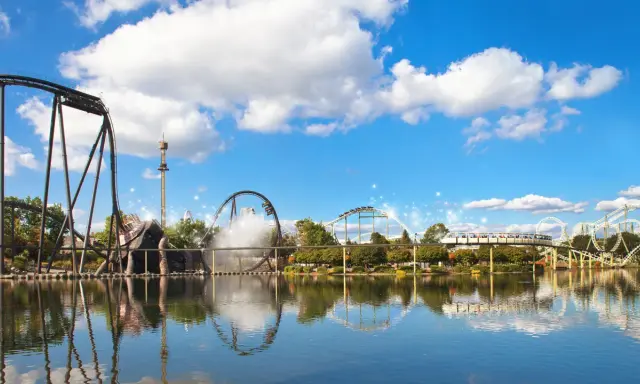 Aussicht auf Achterbahnen und einen Freizeitpark mit Spiegelung im Wasser.