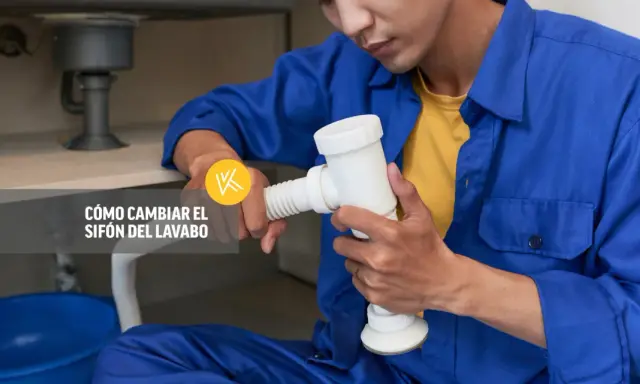Un fontanero realiza la instalación del sifón del lavabo, sujetando la pieza blanca con ambas manos.