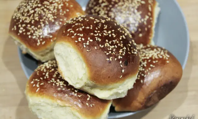 Pięć puszystych bułek do burgerów, posypanych sezamem, ułożonych na talerzu. Idealne na domowe burgery.