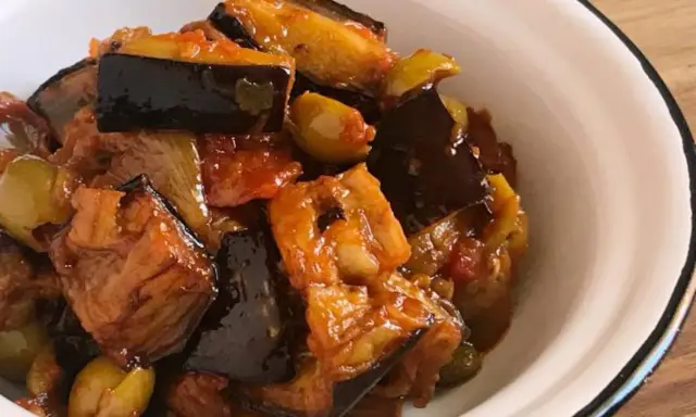 Un plato de caponata siciliana, con berenjenas, aceitunas y tomate, servido en un cuenco blanco.