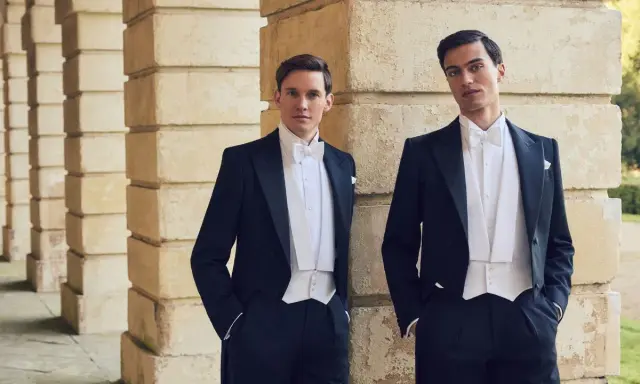 Two men in formal attire, a white tie event, stand by a stone colonnade.