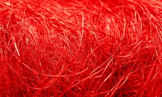 Un groviglio di fili rossi vibranti, una **fibra artificiale** che ricorda un nido intricato o capelli mossi dal vento.