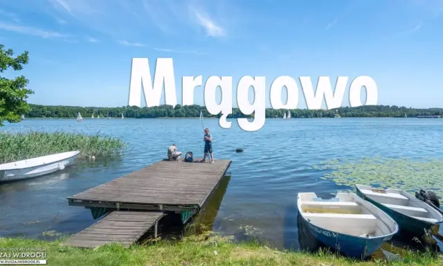 Mrągowo atrakcje: spokojny dzień nad jeziorem, dzieci łowią ryby z pomostu, żaglówki na horyzoncie.