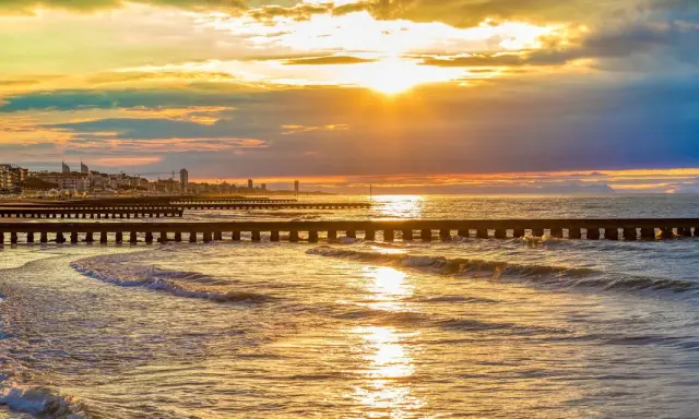 Tramonto dorato sul mare veneto, con moli che si estendono nell'acqua e una città all'orizzonte.