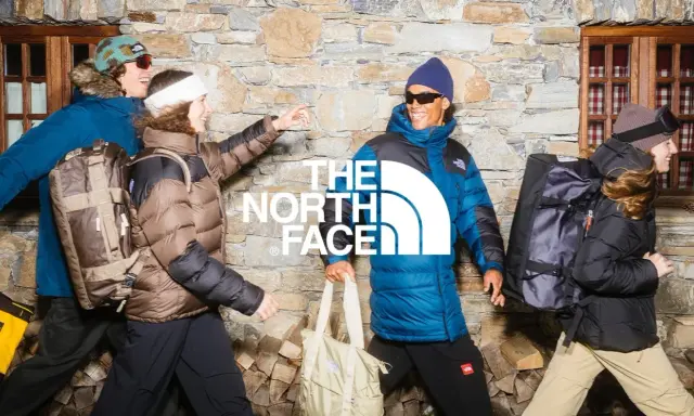 Cztery osoby w kurtkach The North Face, z plecakami i torbami, na tle kamiennej ściany. Jak rozpoznać podróbkę? Sprawdź detale!