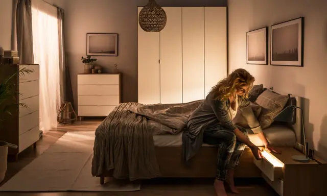 Kobieta szuka czegoś w szufladzie nocnej, która jest podświetlana. Idealna lampa do sypialni powinna tworzyć taki przytulny nastrój.
