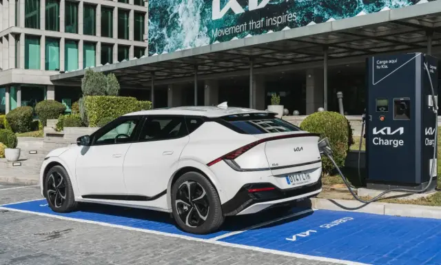 Un coche eléctrico blanco Kia EV6 cargando en un punto Kia Charge. Merece la pena un coche eléctrico por su tecnología y futuro.