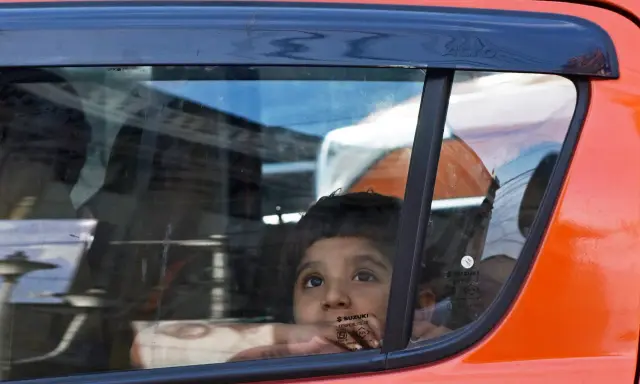 Niño mira por la ventana del coche, apoyado en el cristal, sin silla en el coche. Reflejos en el vidrio.