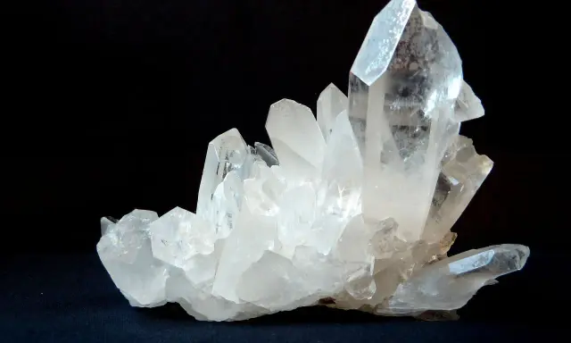 Un grappolo di cristalli di quarzo trasparenti e luminosi su sfondo scuro. Questo è un esempio di che cos'è il quarzo, un minerale comune e versatile.