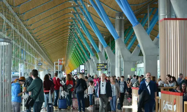 Ludzie z bagażami w nowoczesnym terminalu, jednym z wielu lotnisk w Europie, podziwiają architekturę z kolorowymi podporami.