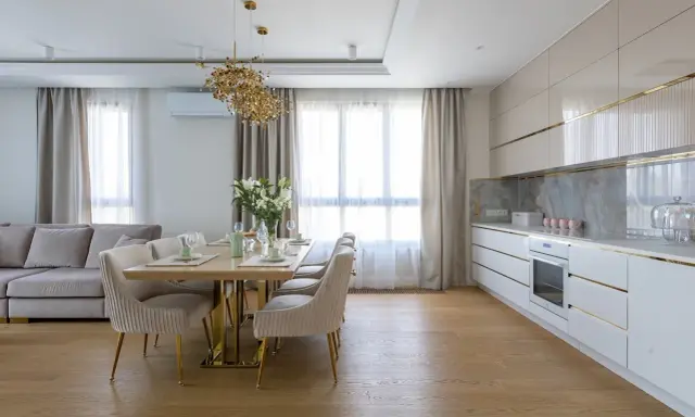 Elegancka kuchnia w stylu modern classic z jadalnią. Jasne meble, złote detale i wygodna sofa tworzą przytulną atmosferę.