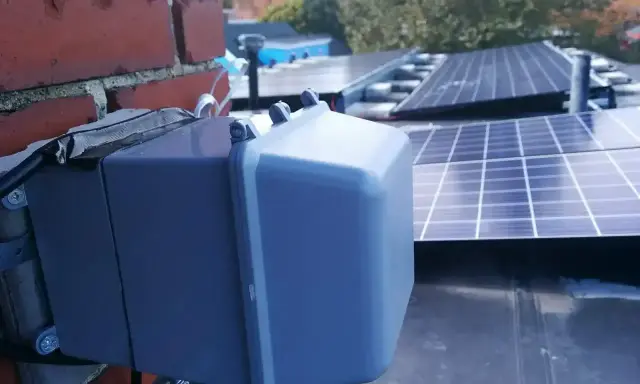 System podgrzewania paneli fotowoltaicznych zamontowany na dachu, obok ceglanej ściany.