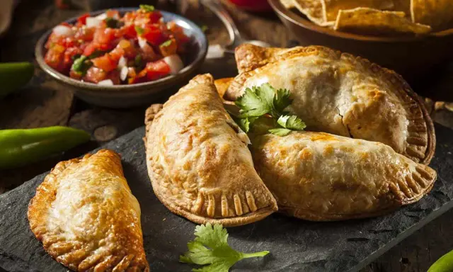 Gyllene argentinska empanadas recept på en svart stenplatta, serverade med färsk salsa och tortillachips.