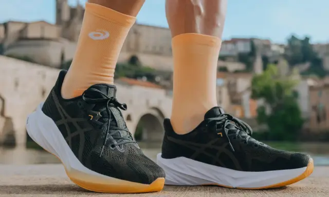 Biegacz w pomarańczowych skarpetkach z logo Asics i ciemnych butach tej firmy, gotowy do podboju miasta.