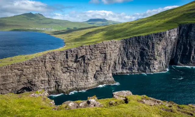 Scogliere imponenti e un lago blu intenso nelle Isole Faroe, dove gli abitanti vivono in armonia con la natura selvaggia.