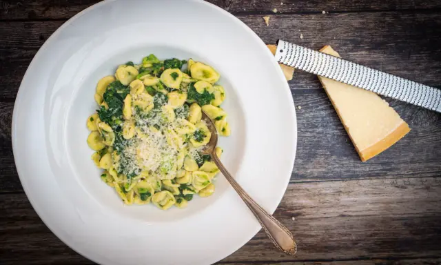 Orecchiette mit Cime di Rapa, frisch geriebenem Parmesan und einem Löffel auf einem Holztisch.