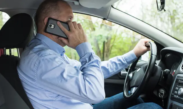Mężczyzna za kierownicą rozmawia przez telefon, co może skończyć się mandatem.