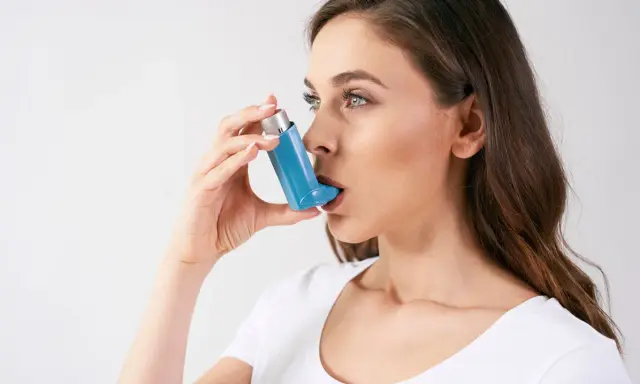 Frau benutzt einen blauen Inhalator gegen Allergien, um ihre Lunge zu befreien.