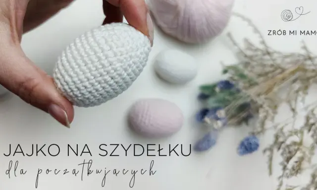 Ręcznie robione, białe jajko na szydełku, idealne na początek przygody z szydełkowaniem. W tle pastelowe włóczki i suszone kwiaty.
