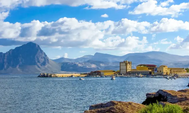 La tonnara di Bonagia, con il suo porto e le montagne sullo sfondo, sotto un cielo azzurro e nuvoloso.