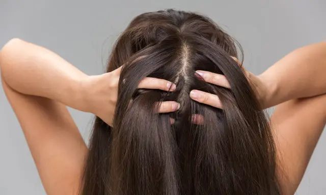 Une femme se touche les cheveux, montrant comment hydrater son cuir chevelu pour des cheveux sains et brillants.