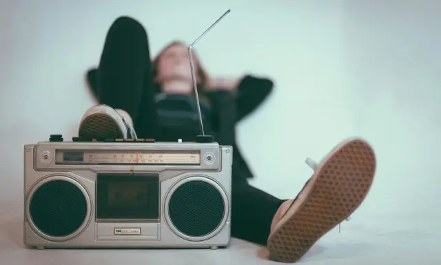 Osoba relaksuje się przy radiomagnetofonie, słuchając muzyki. To pokazuje, jak łatwo dotrzeć do odbiorców, co jest jedną z **zalet reklamy radiowej**.
