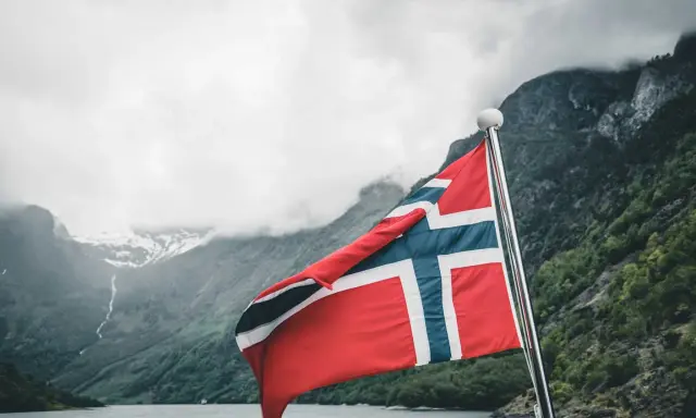 Norweska flaga na tle fiordu. Marzenia o wysokich zarobkach w Norwegii stają się rzeczywistością.