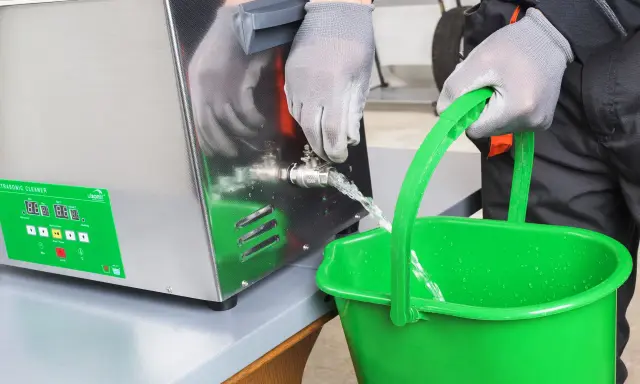 Wylewanie płynu z myjki ultradźwiękowej do zielonego wiadra.
