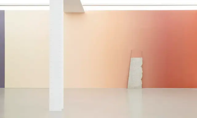 A gallery wall features a stunning gradient in art, transitioning from soft peach to warm coral. A rough stone slab leans against it.