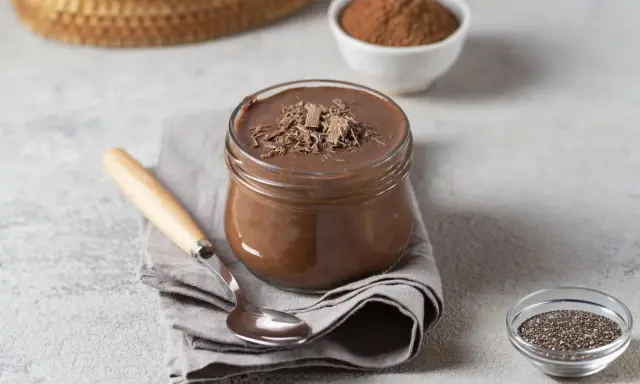 Pudding proteinowy z czekoladą, idealny na deser. Obok nasiona chia i kakao, sugerujące, z czym jeść.