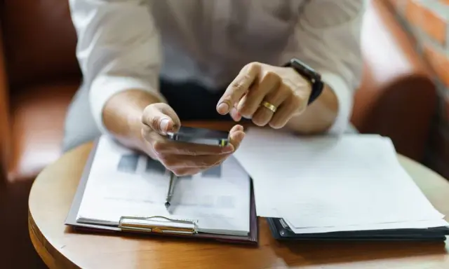 Hombre revisa su móvil, con documentos de modelo fin de contrato de alquiler y entrega de llaves sobre la mesa.