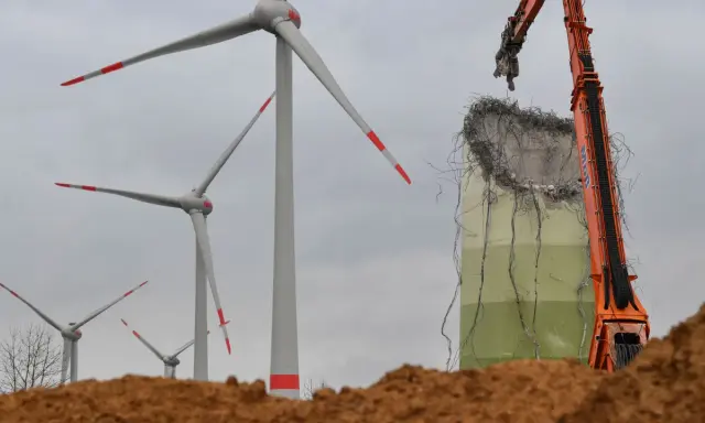 Abrissbagger demontiert eine Windkraftanlage. Im Hintergrund stehen noch weitere Windräder, die ihre lange Laufzeit hinter sich haben.