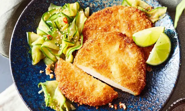 Knuspriges Kohlrabi-Schnitzel mit Gurkensalat und Limettenspalten auf blauem Teller.