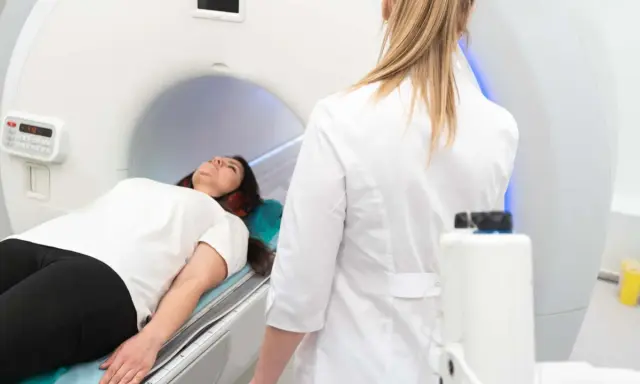 Patient liegt auf dem Tisch für die pelottierung des duralschlauches. Eine Ärztin in weißem Kittel überwacht den Vorgang.