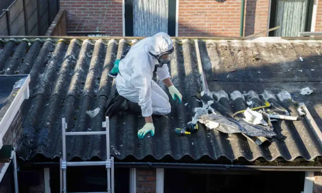 Travailleur en combinaison intégrale sur un toit en fibrociment, préparant le terrain pour une nouvelle peinture. Quelle peinture pour recouvrir peinture au plomb ?