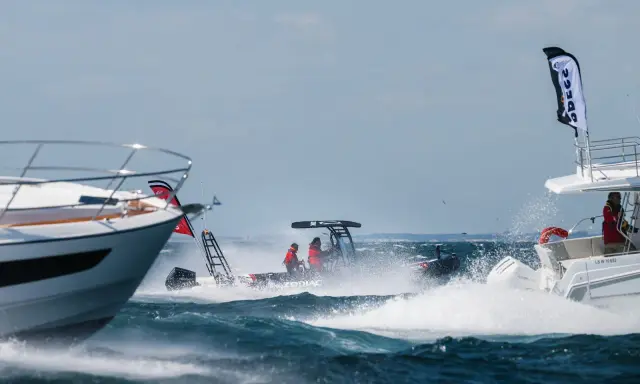 Trois bateaux en pleine navigation, éclaboussures d'eau, ciel bleu. L'un d'eux, un Zodiac, fend les vagues avec deux personnes à bord.