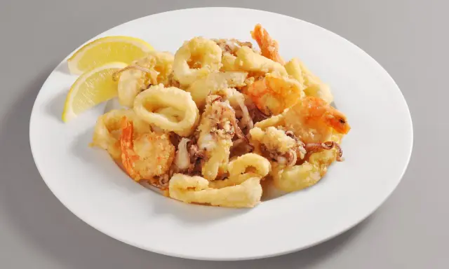 Un invitante piatto di frittura di pesce, con anelli di calamari dorati e gamberi croccanti, guarnito con spicchi di limone fresco.