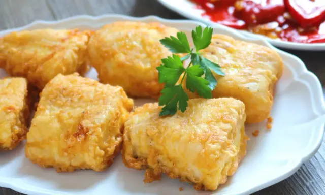 Merluza a la romana dorada y jugosa en un plato blanco con perejil.
