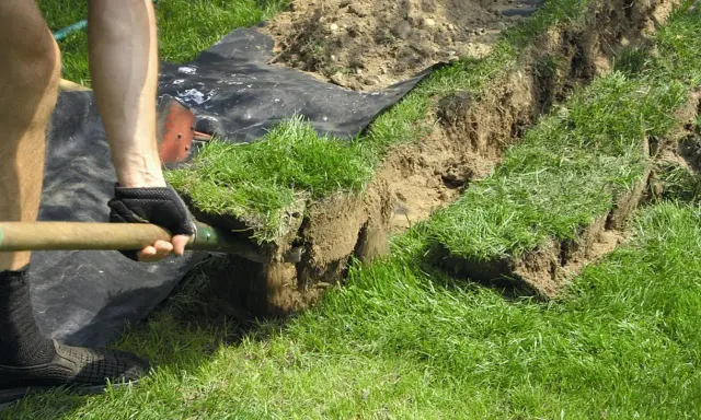 Osoba kopie rów, przygotowując teren pod układanie kabli w ziemi zgodnie z normą.