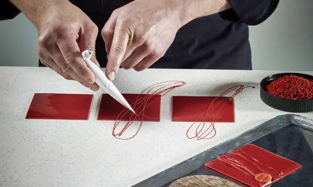 Mains travaillant avec du chocolat plastique rouge pour décorer des carrés de glaçage.