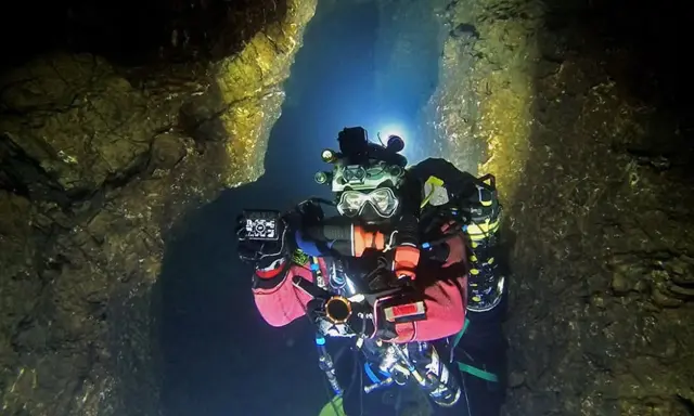 Plongée dans une grotte sous-marine, Xavier Meniscus filme les parois rocheuses éclairées par ses lampes.