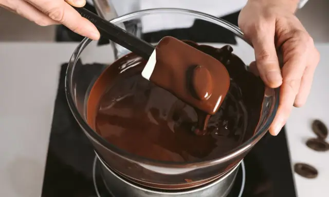 Un chocolat qui ne fond pas ? Ce n'est pas le cas ici ! Une spatule mélange du chocolat fondu brillant dans un bol en verre au-dessus d'un bain-marie.