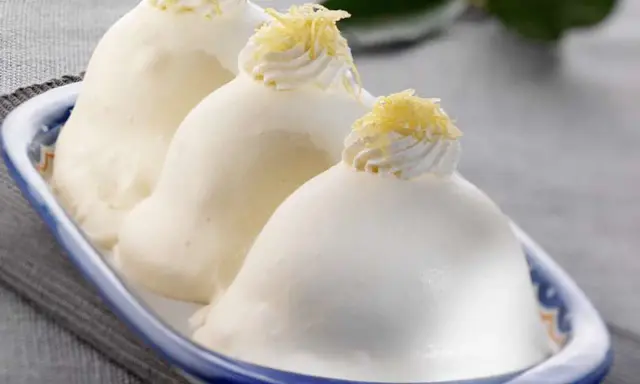 Tre deliziose delizie al limone, guarnite con panna e scorza di limone, in un piatto blu e bianco.