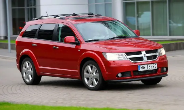 Czerwony Dodge Journey 3.6 z bagażnikiem dachowym jedzie po brukowanej drodze.